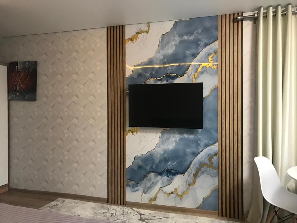 A room with a mounted flat-screen TV, patterned wall, and a white chair.