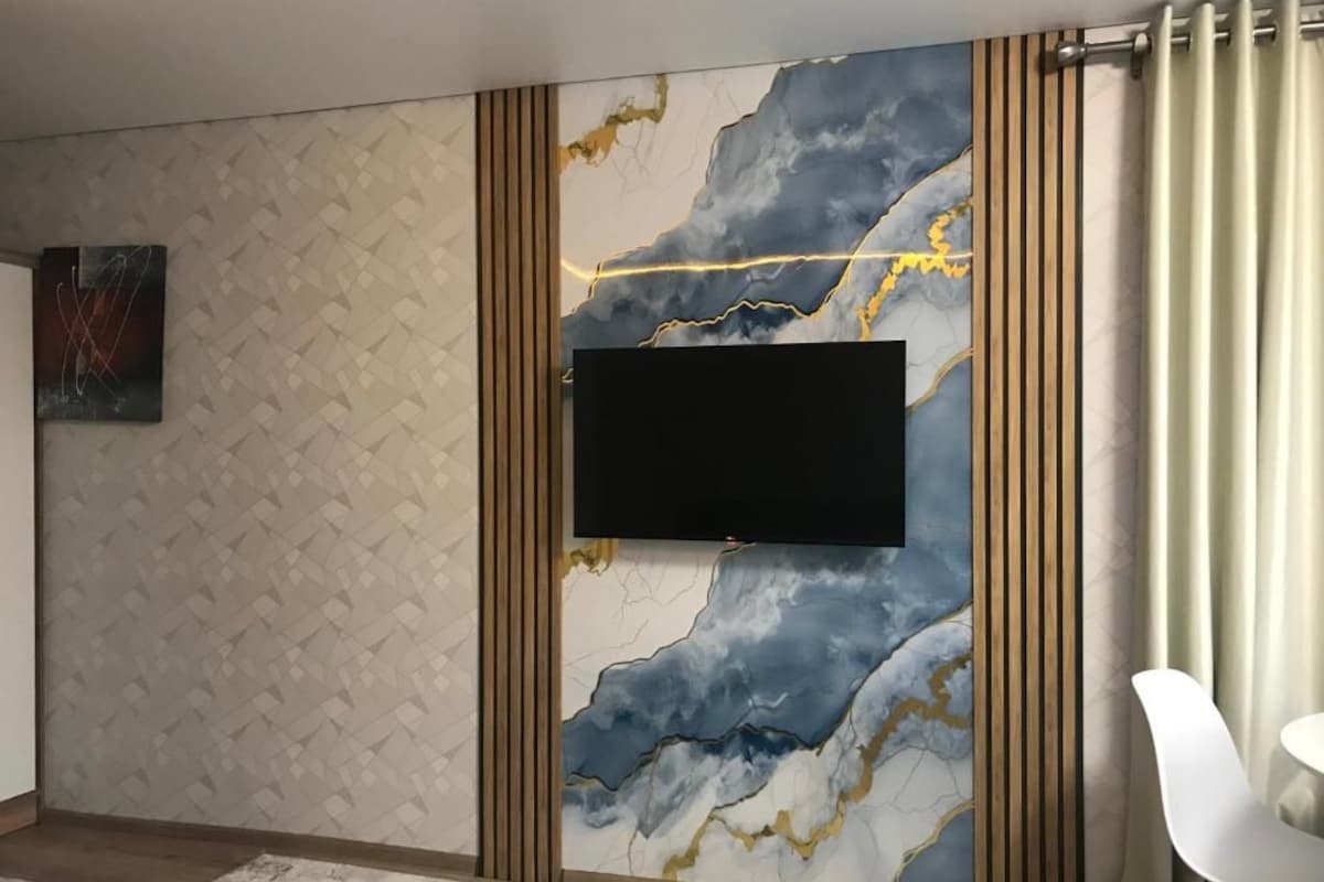 A room with a mounted flat-screen TV, patterned wall, and a white chair.