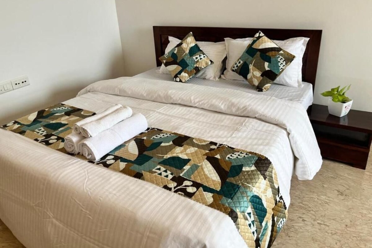 A hotel room with a bed, a nightstand, and a potted plant.