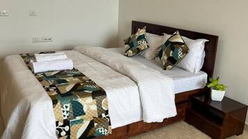 A neatly made bed with a quilt and pillows, a bedside table with a plant, and a power outlet on the wall.