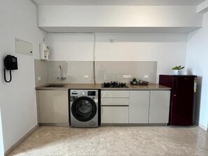A compact kitchen with a washing machine, a sink, and a refrigerator. - Luna Spaces Riva (mumbai)