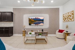 Een moderne woonkamer met een flatscreen televisie aan een muur, een salontafel, een bank en een keuken met donkere kastjes.