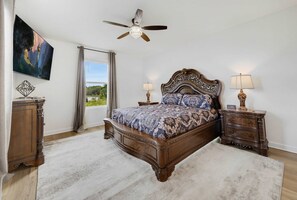 A bedroom with a large bed, two bedside tables, a ceiling fan, and a painting on the wall. - 100 TV - Pool Spa Epic Game Room Villa for 14 (Kissimmee)