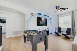 A room with a foosball table, a television mounted on a wall, and a ceiling fan. - 100 TV - Pool Spa Epic Game Room Villa for 14 (Kissimmee)