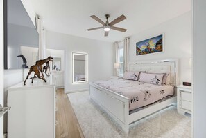Quarto com cama, ventilador de teto, pintura e escultura de girafa.