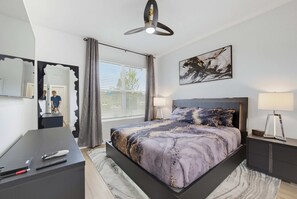 A modern bedroom with a bed, bedside table, lamp, and artwork. - 100 TV - Pool Spa Epic Game Room Villa for 14 (Kissimmee)
