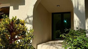 A pathway leading to a building entrance with an arched doorway, surrounded by greenery and a stone-paved area.