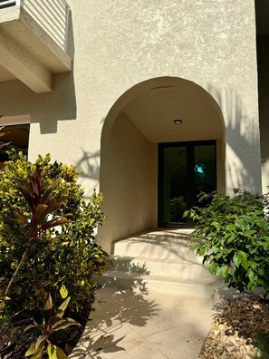 A pathway leading to a building entrance with an arched doorway, surrounded by greenery and a stone-paved area. - Kokomo Keys - Waterfront Heated Pool (Summerland Key)