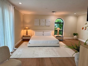 A bedroom with a large bed, two bedside tables with lamps, a window with a view of greenery, and a white rug. - Kokomo Keys - Waterfront Heated Pool (Summerland Key)