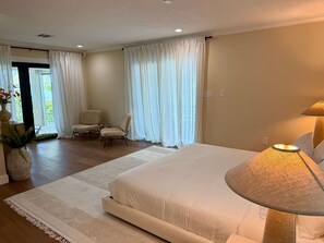 A bedroom with a large bed, two chairs, a lamp, and a view of greenery outside. - Kokomo Keys - Waterfront Heated Pool (Summerland Key)