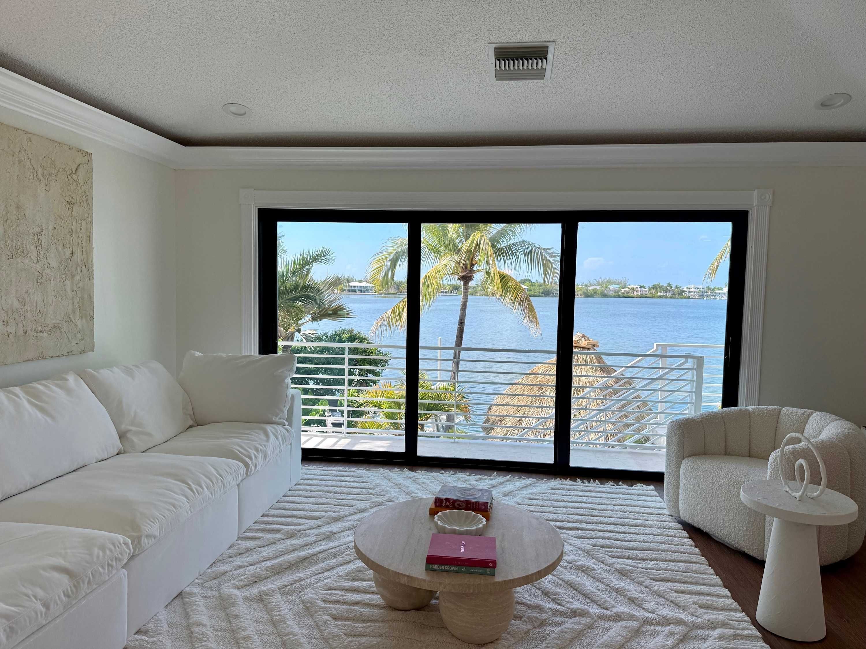 A modern living room with a white sofa, a round coffee table with books, and a view of a body of water through large windows.