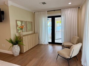 A hotel room with a wooden floor, a seating area with two chairs, a large window with curtains, and a wall-mounted TV. - Kokomo Keys - Waterfront Heated Pool (Summerland Key)