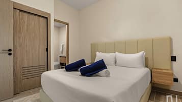 A hotel room with a bed, a wooden door, a nightstand, and a bathroom visible through an open door.