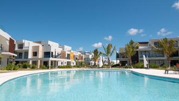 A clear blue swimming pool surrounded by modern buildings with balconies, under a clear sky.