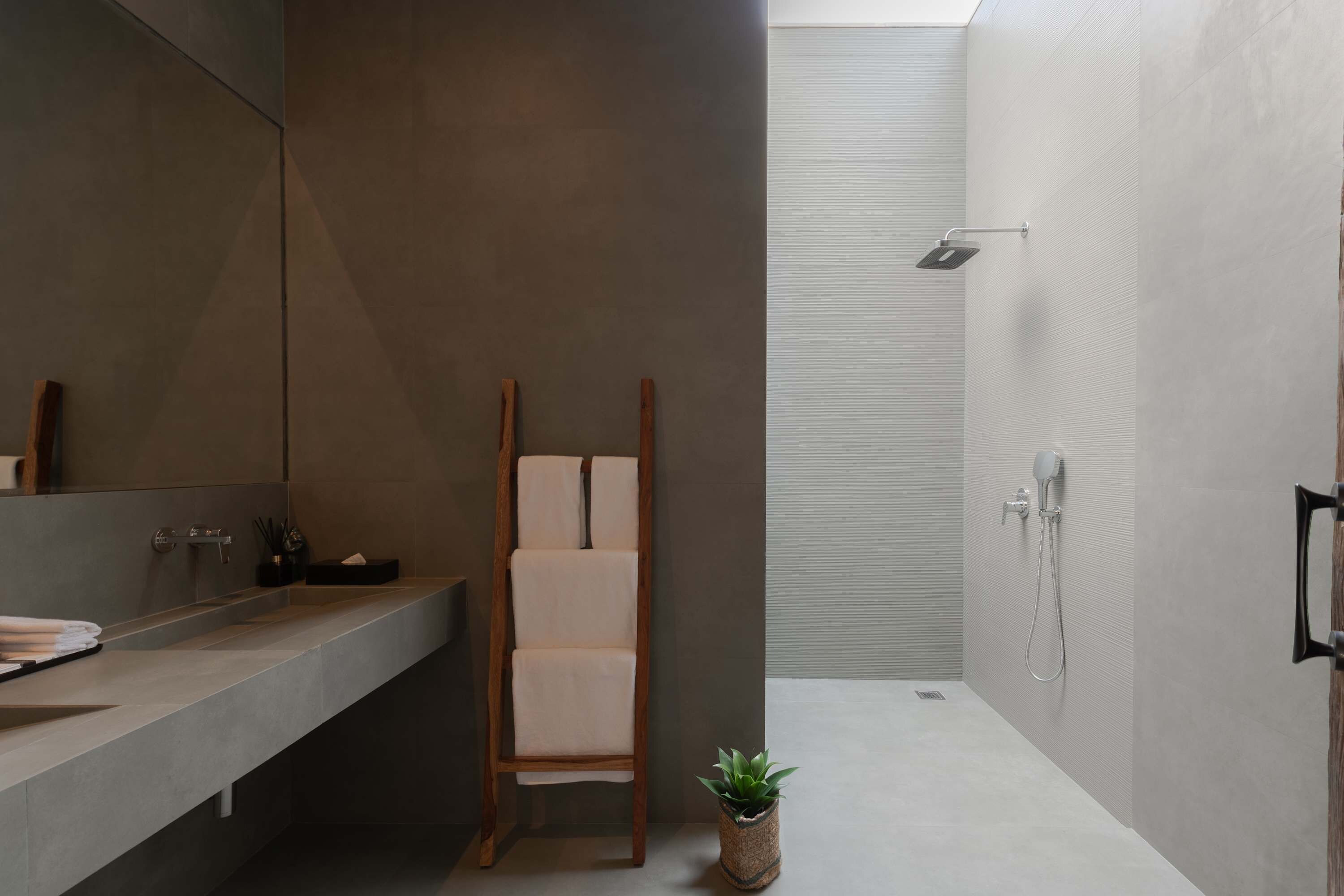 Un baño moderno con un espejo grande, una silla de madera, una planta pequeña y una zona de ducha.
