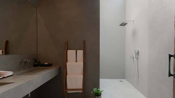 Un baño moderno con un espejo grande, una silla de madera, una planta pequeña y una zona de ducha.