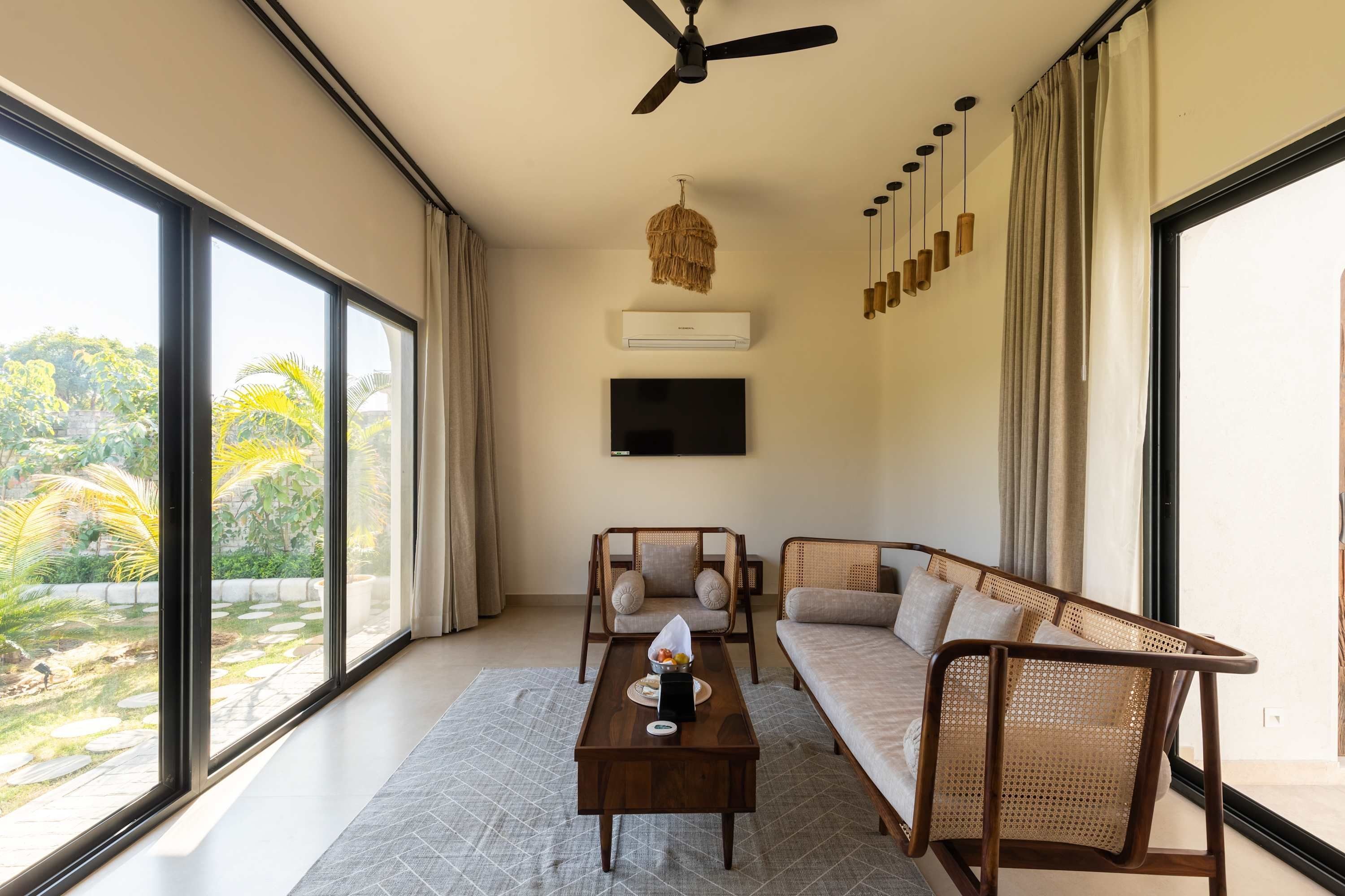 A spacious living room with a large window, a ceiling fan, a flat-screen TV, and a dining area with a table and chairs.