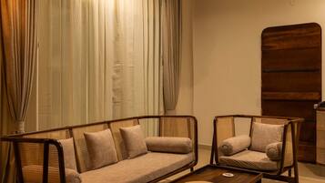 Una sala de estar moderna con un sofá y dos sillones, un aparador de madera y un ventanal con cortinas.