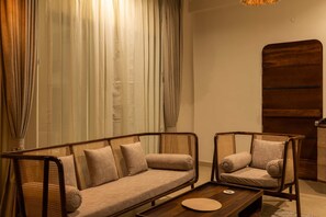 A modern living room with a sofa and two armchairs, a wooden sideboard, and a large window with curtains.