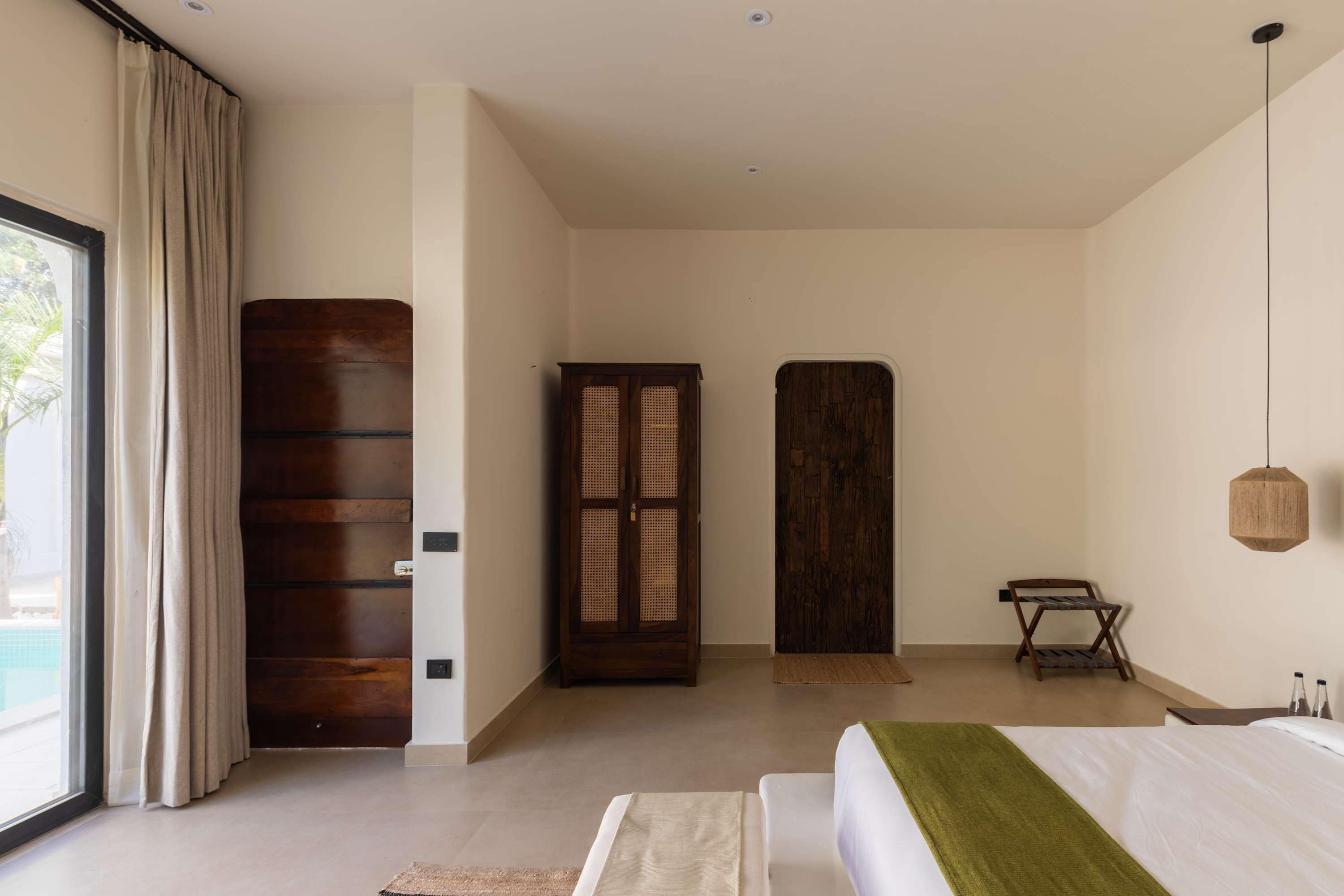 A bedroom with a bed, a wooden wardrobe, a door, and a window with curtains.