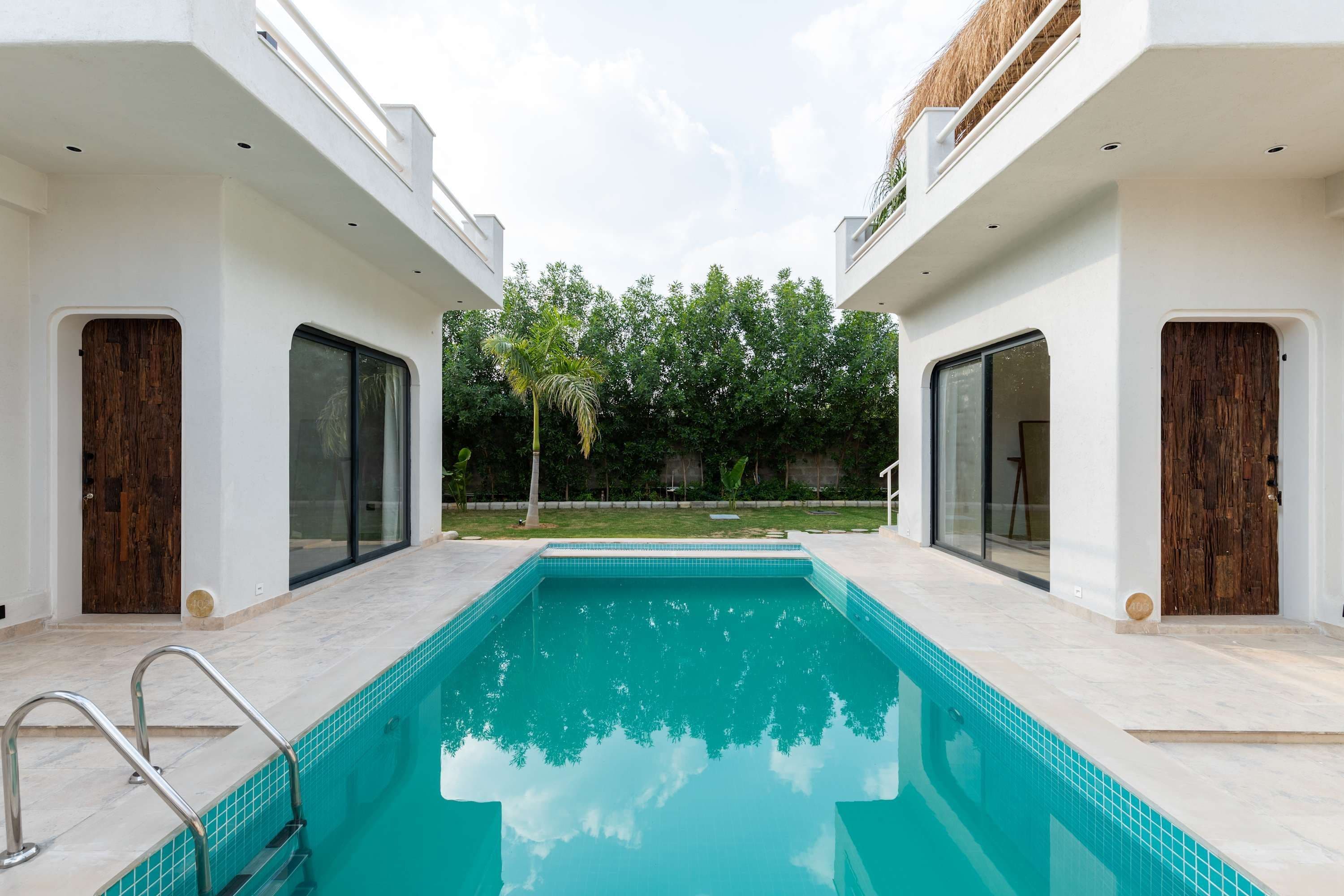 A modern pool area with a clear blue pool, white walls, and wooden doors.