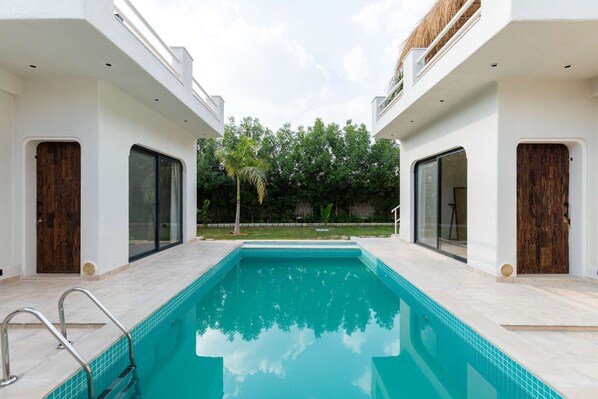 A modern pool area with a clear blue pool, white walls, and wooden doors.