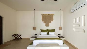 A hotel room with a bed, bedside tables, a hanging macrame wall decoration, a ceiling fan, and an air conditioning unit.