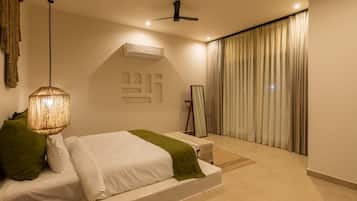 A modern bedroom with a bed, a hanging light fixture, an air conditioning unit, a mirror, and a view of the outdoors through curtains.