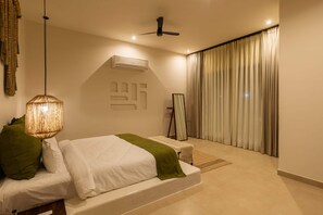 A modern bedroom with a bed, a hanging light fixture, an air conditioning unit, a mirror, and a view of the outdoors through curtains.