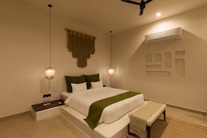 Une chambre à coucher moderne, comprenant un lit, des tables de chevet, un banc et un climatiseur fixé au mur.