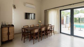 A dining area with a large table and chairs, a flat-screen TV mounted on the wall, and a sliding glass door leading to an outdoor pool area.