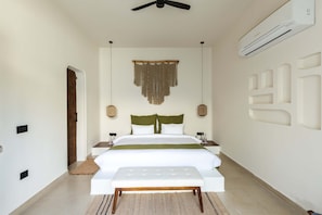 A bedroom with a bed, bedside tables, a bench, a ceiling fan, an air conditioning unit, and a wall-mounted light fixture. - La Vida Retreat - Luxe 2 Bed Villa in Jaipur (Jaipur)