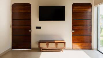 Una habitación con una televisión de pantalla plana grande montada en la pared, un mueble de madera con frente de ratán y dos puertas de madera con pomos de metal.