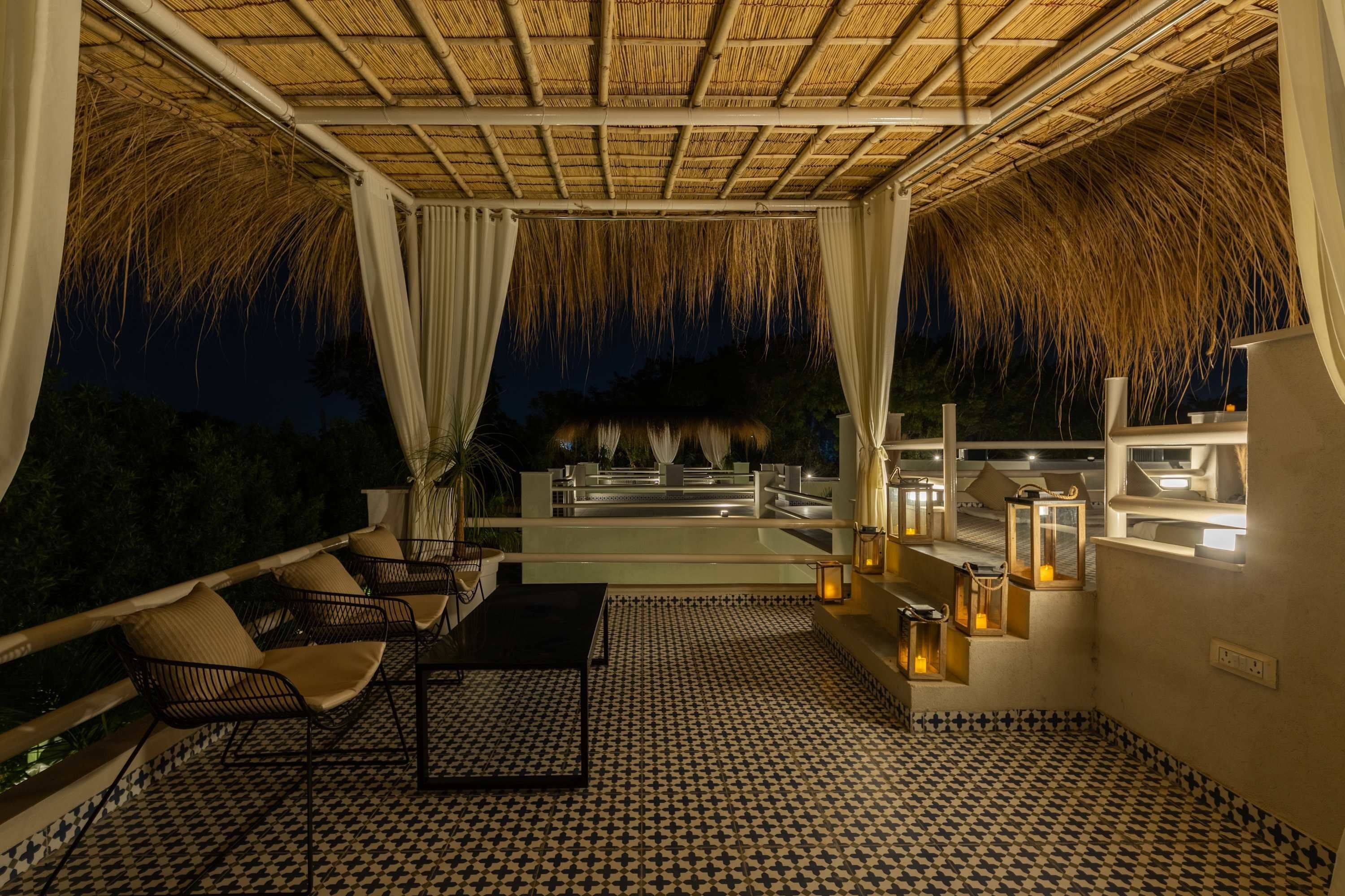A terrace with a thatched roof, outdoor seating, and ambient lighting.