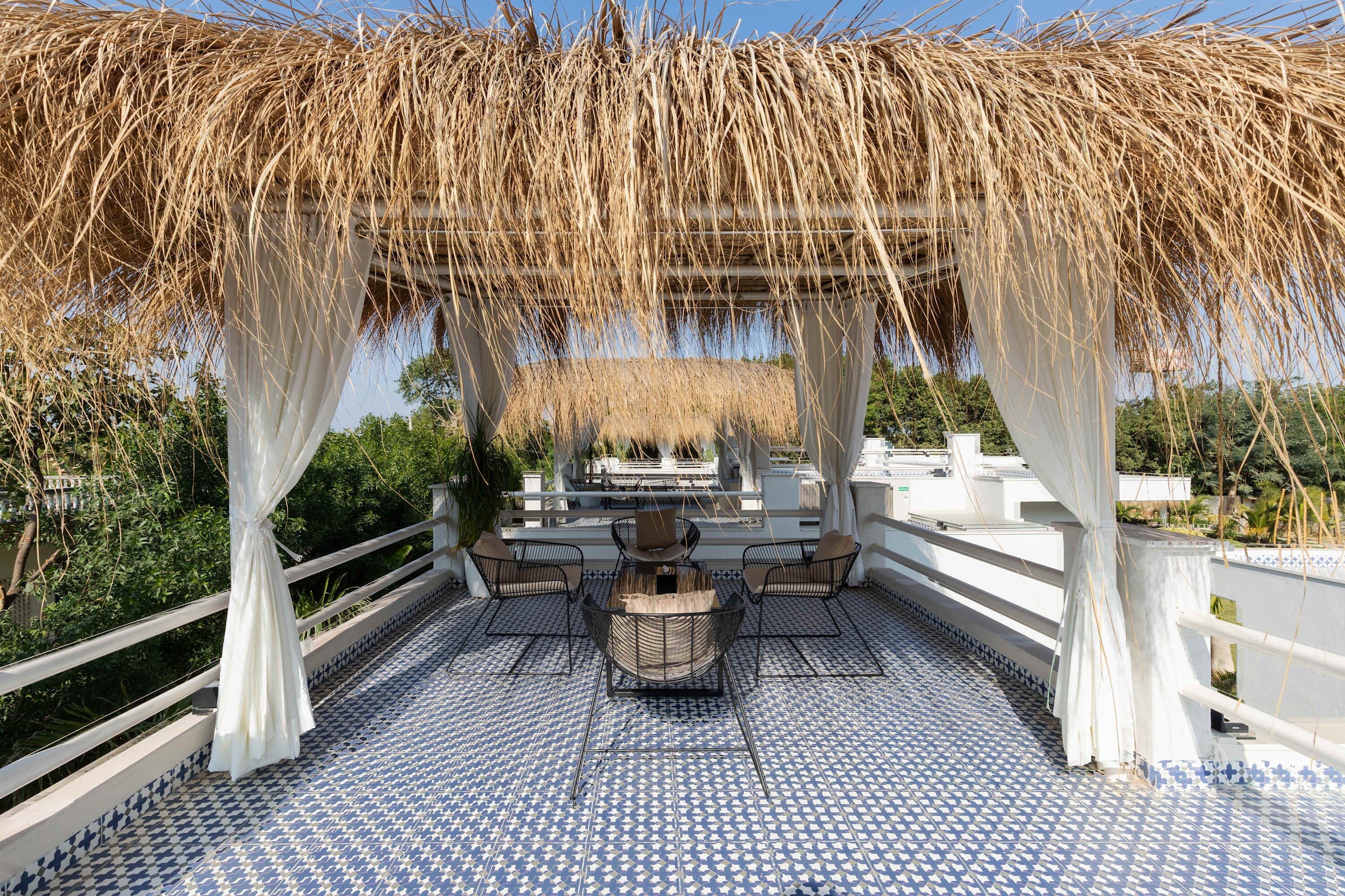 Un patio exterior con suelo de baldosas estampadas, una mesa con sillas y una pérgola con plantas colgantes.