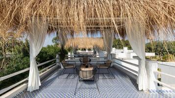 Un patio exterior con suelo de baldosas estampadas, una mesa con sillas y una pérgola con plantas colgantes.