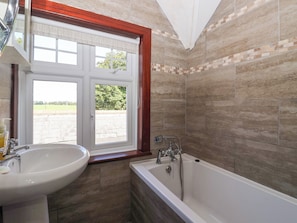 Ein Badezimmer mit einer Badewanne, einem Waschbecken und einem Fenster mit Blick auf eine Ziegelwand und Grünflächen.