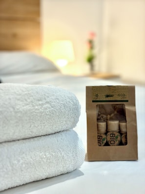 A stack of white towels and a package of organic bath products on a white surface. - Nice room with a private bathroom in Arco del Triunfo, Downtown (Barcelona)
