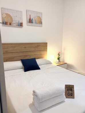 Ein ordentlich bezogenes Bett mit weißen Leinentüchern, einem Holz-Kopfschild und einem blauen Kopfkissen.