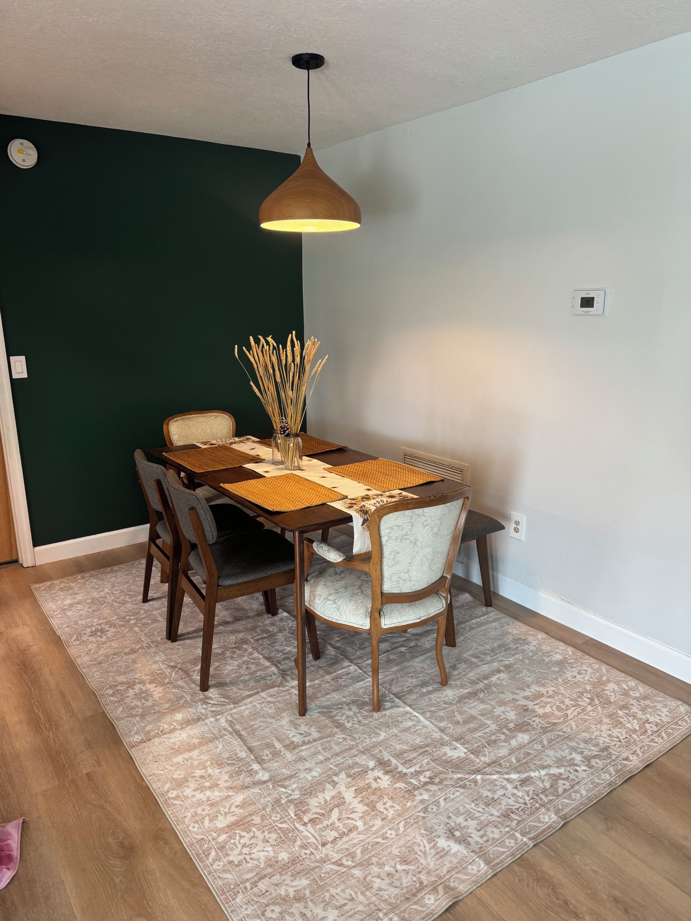 A dining area with a table, chairs, a hanging light fixture, and a decorative vase.