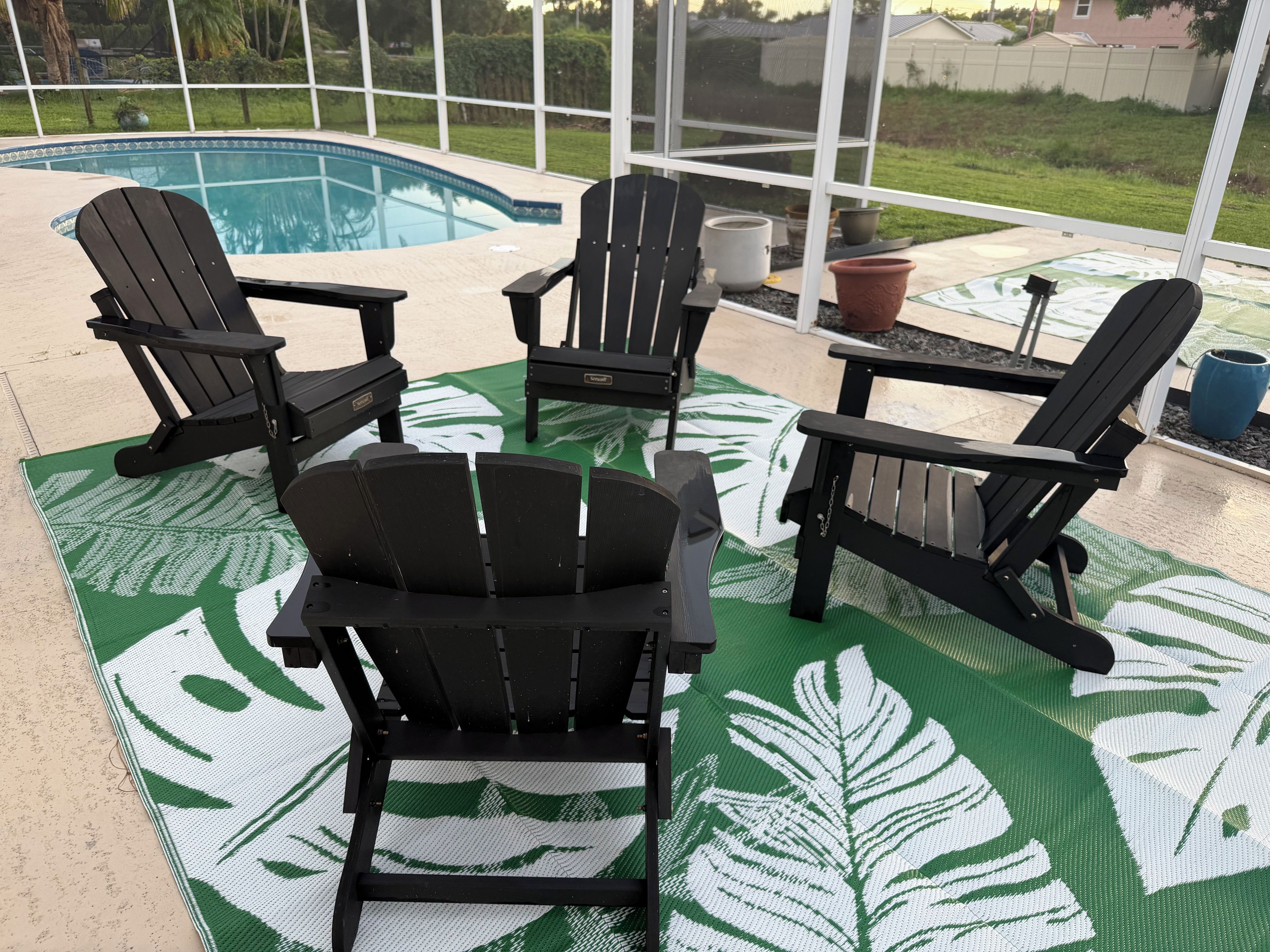 Área da piscina com quatro cadeiras Adirondack e um tapete estampado em verde.