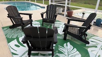 Área da piscina com quatro cadeiras Adirondack e um tapete estampado em verde.
