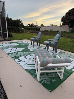 An outdoor seating area with a green patterned mat, two chairs, and a lounge chair. -     Casa del Sol PSL — Newly Remodeled Pool Retreat (Port St. Lucie)