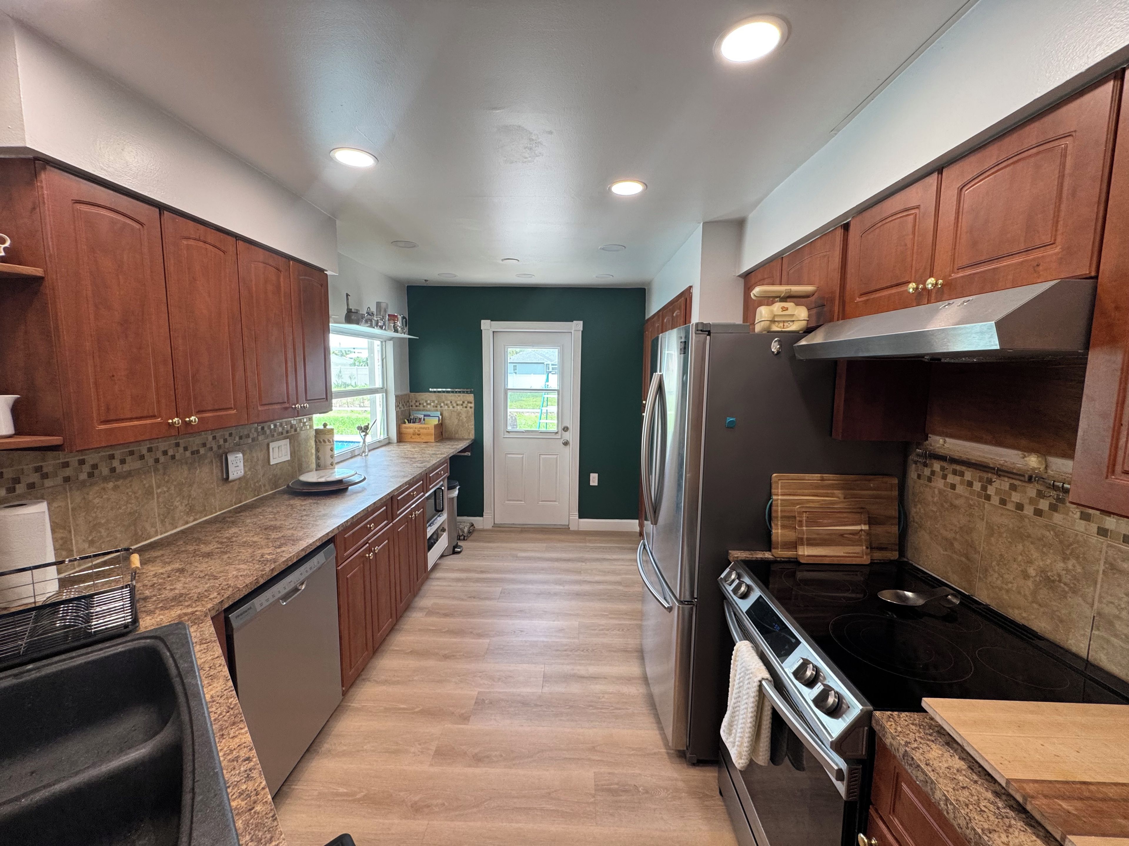 A modern kitchen with wooden cabinets, a stainless steel refrigerator, and a black stove.