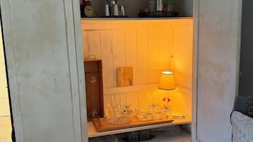 A room with a vintage-style cabinet with open doors, revealing a shelf with various items and a lit lamp.