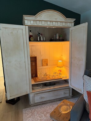 A room with a vintage-style cabinet with open doors, revealing a shelf with various items and a lit lamp.