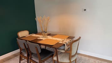 A dining area with a wooden table, two chairs, a vase with dried plants, and a pendant light.