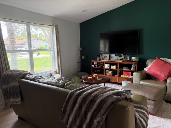 A living room with a sofa, armchair, coffee table, and a TV on a wall.