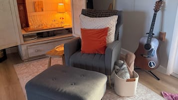 A living room with a grey armchair, ottoman, and a guitar against the wall.
