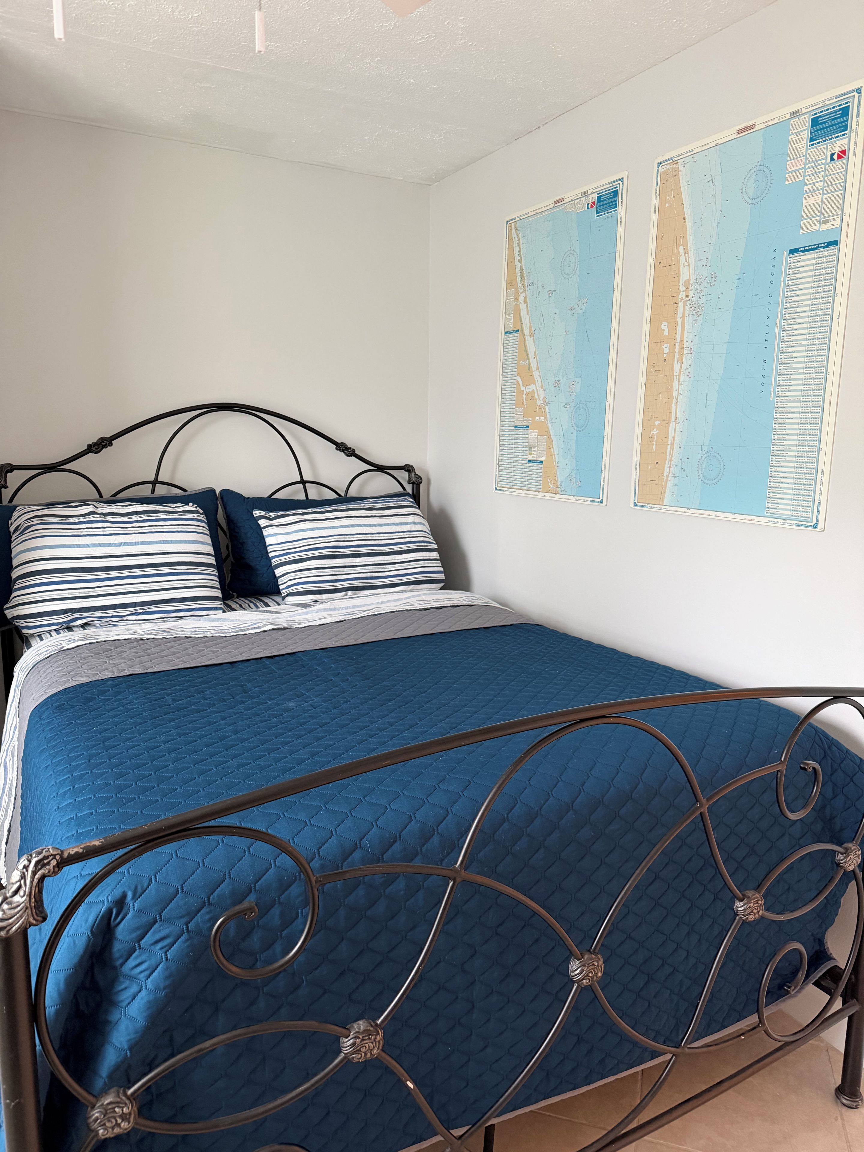 A bed with a blue quilt and metal frame, a striped pillow, and two wall maps.